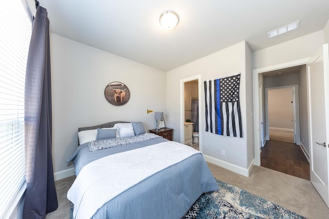 carpeted bedroom featuring visible vents, baseboards, and ensuite bath