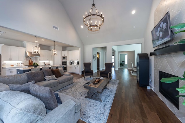 living room with high vaulted ceiling, visible vents, dark wood-type flooring, a high end fireplace, and a chandelier