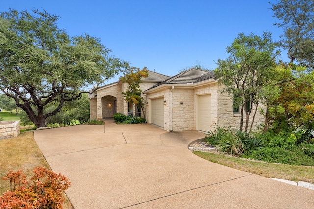 view of front of property featuring concrete driveway, stone siding, an attached garage, and a tiled roof