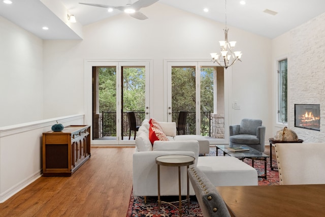 living area featuring vaulted ceiling, a stone fireplace, wood finished floors, and a notable chandelier