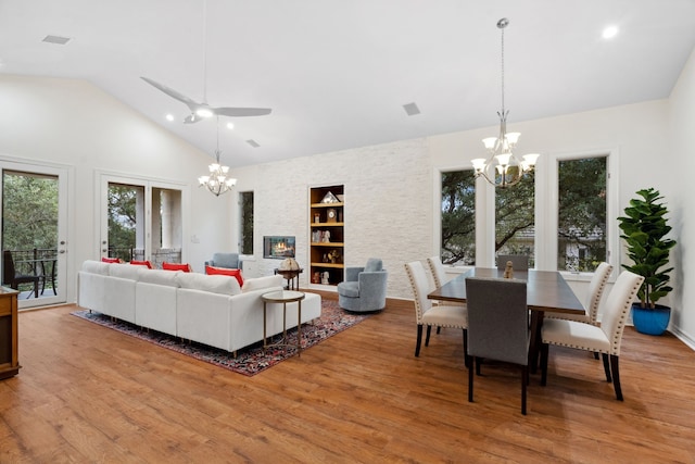 living room with a stone fireplace, built in shelves, high vaulted ceiling, and wood finished floors