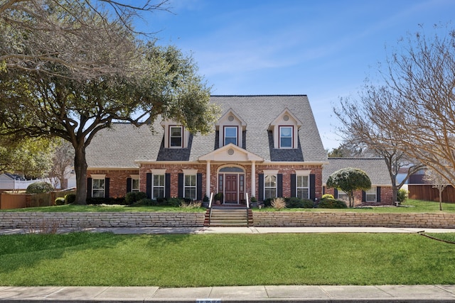 cape cod home featuring a shingled roof, brick siding, fence, and a front lawn