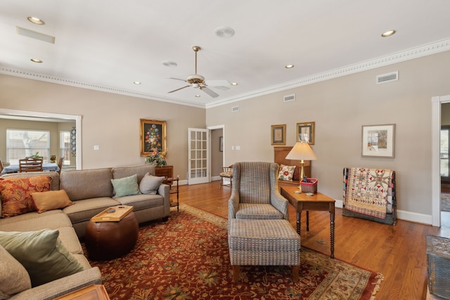 living area with baseboards, wood finished floors, visible vents, and crown molding