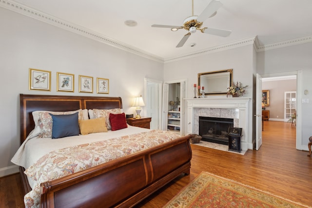 bedroom featuring a fireplace, ornamental molding, ceiling fan, wood finished floors, and baseboards