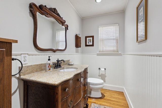 half bath featuring a wainscoted wall, vanity, wood finished floors, and toilet