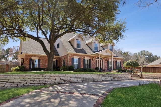 new england style home featuring roof with shingles, fence, and brick siding