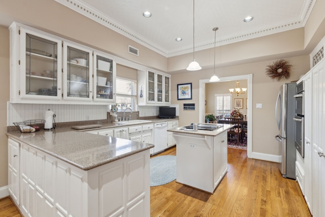 kitchen featuring visible vents, appliances with stainless steel finishes, glass insert cabinets, a peninsula, and a sink