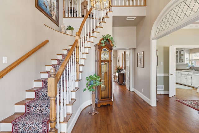 foyer with visible vents, baseboards, a towering ceiling, wood finished floors, and a notable chandelier