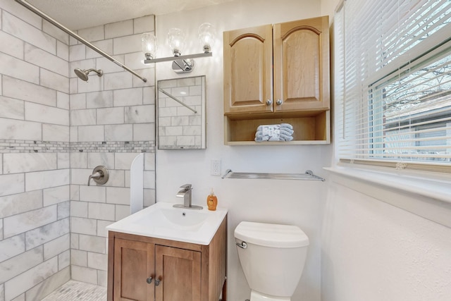 bathroom featuring tiled shower, toilet, and vanity