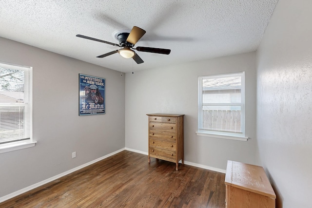 unfurnished bedroom with multiple windows, a textured ceiling, baseboards, and dark wood-style flooring