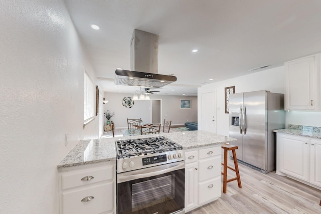 kitchen with island exhaust hood, appliances with stainless steel finishes, white cabinets, and light wood finished floors