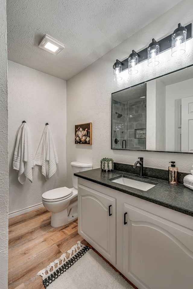 bathroom with toilet, a stall shower, a textured ceiling, wood finished floors, and a textured wall