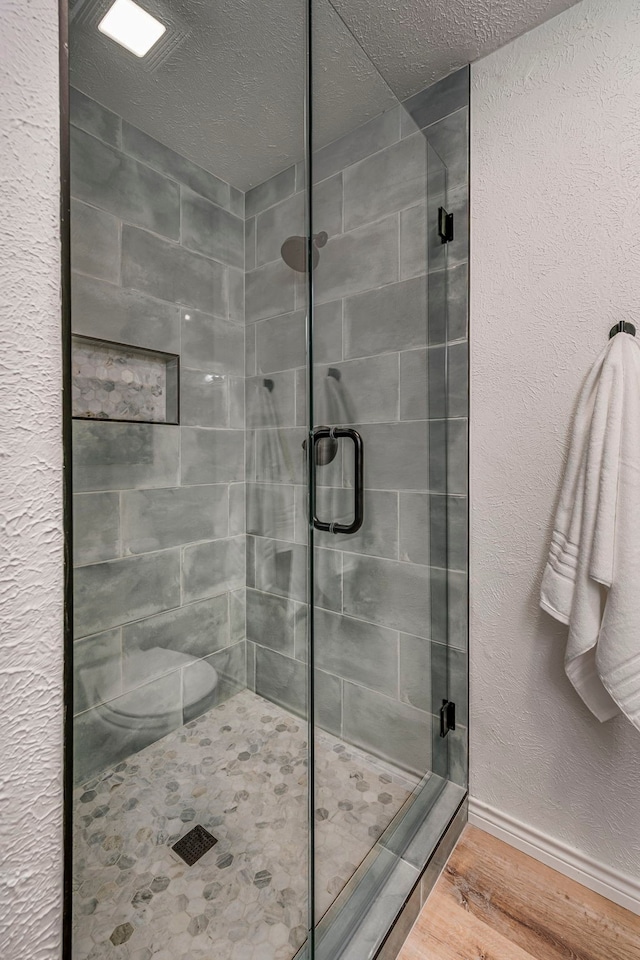 bathroom featuring a stall shower, baseboards, wood finished floors, and a textured wall