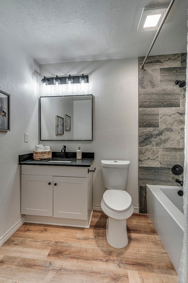 bathroom featuring toilet, a textured ceiling, wood finished floors, washtub / shower combination, and vanity