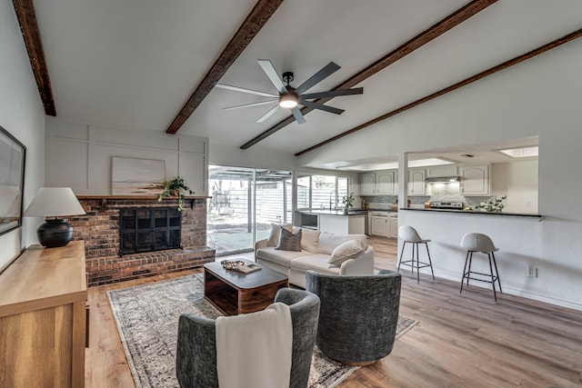 living area featuring light wood finished floors, a fireplace, vaulted ceiling with beams, and ceiling fan