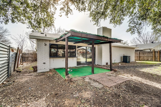 rear view of house with cooling unit, a fenced backyard, brick siding, and a chimney