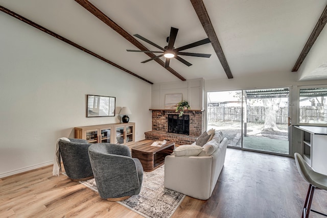 living area with lofted ceiling with beams, a brick fireplace, plenty of natural light, and light wood finished floors