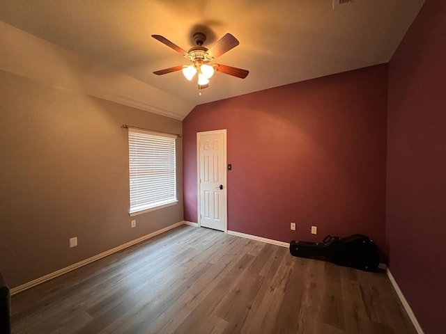 empty room with vaulted ceiling, wood finished floors, a ceiling fan, and baseboards