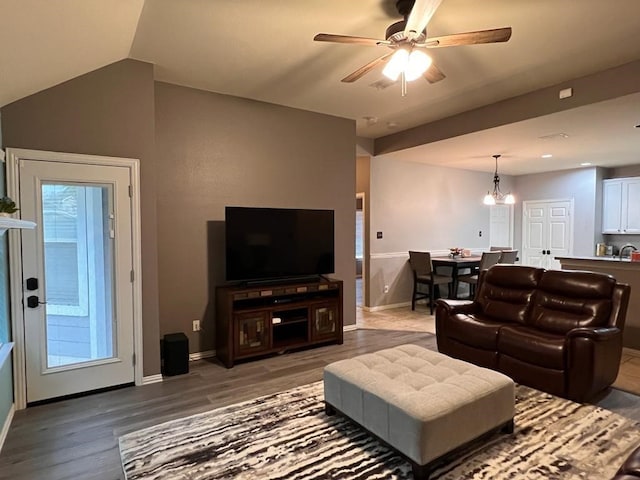 living room featuring lofted ceiling, ceiling fan with notable chandelier, wood finished floors, and baseboards