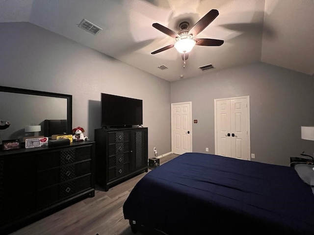 bedroom featuring a ceiling fan, visible vents, vaulted ceiling, and wood finished floors