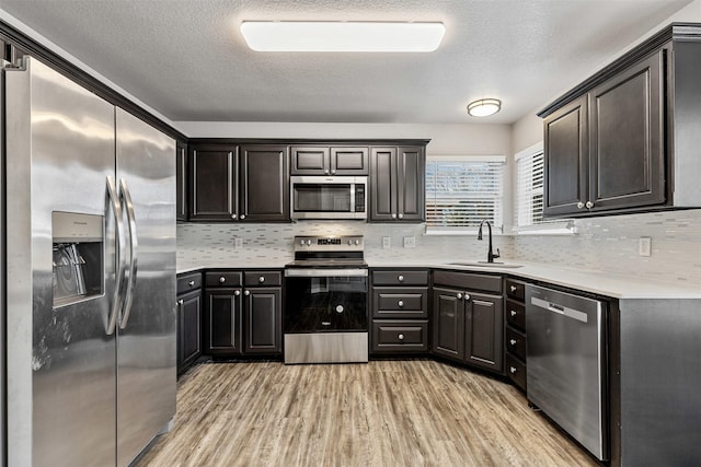 kitchen featuring backsplash, light wood-type flooring, light countertops, stainless steel appliances, and a sink