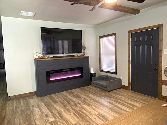 living area with a glass covered fireplace, visible vents, ceiling fan, and wood finished floors