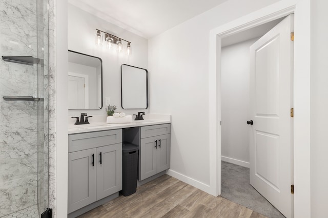 full bath with double vanity, a marble finish shower, a sink, and wood finished floors