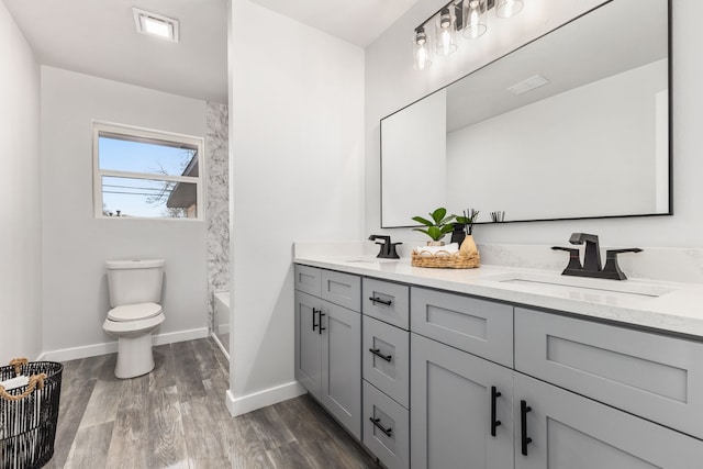 bathroom with double vanity, baseboards, toilet, wood finished floors, and a sink