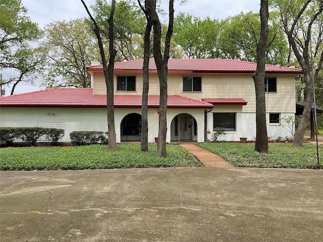 mediterranean / spanish-style house featuring a tiled roof and brick siding