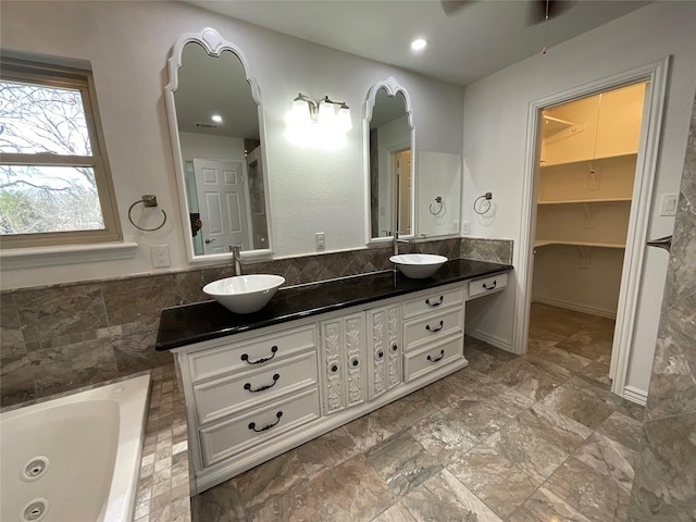 full bath featuring double vanity, a tub with jets, a walk in closet, and a sink