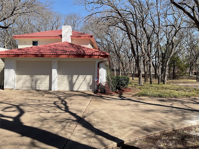 view of side of home with a garage, driveway, a chimney, and a tile roof