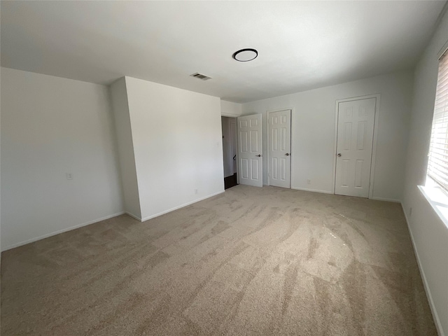 unfurnished bedroom with baseboards, visible vents, two closets, and light colored carpet