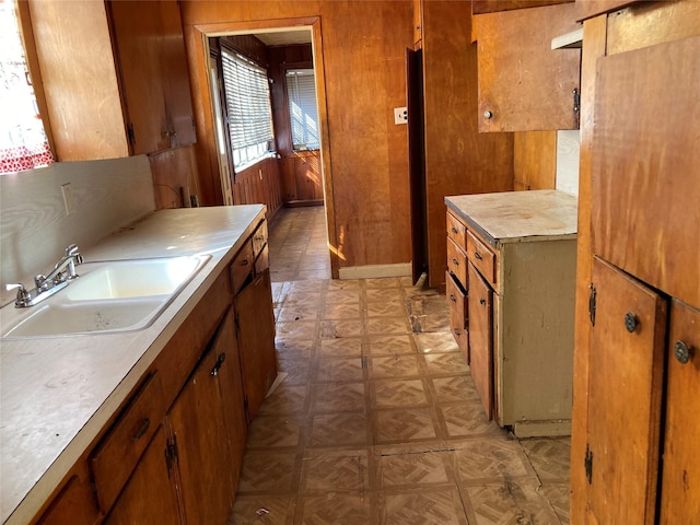 kitchen with wood walls, a sink, light countertops, brown cabinets, and light floors