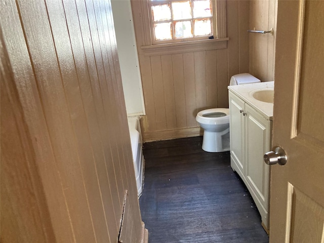 full bathroom featuring toilet, wooden walls, wood finished floors, vanity, and a bath