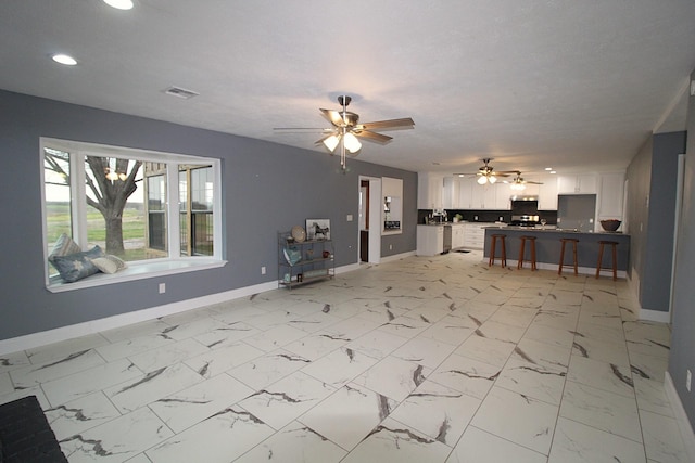 unfurnished living room with ceiling fan, a textured ceiling, visible vents, baseboards, and marble finish floor