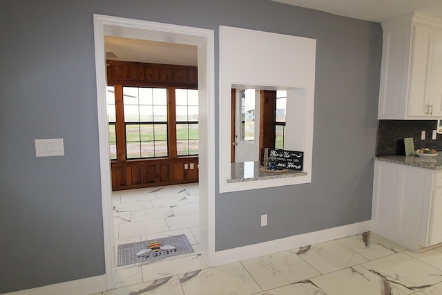 kitchen with light stone countertops, marble finish floor, baseboards, and white cabinetry