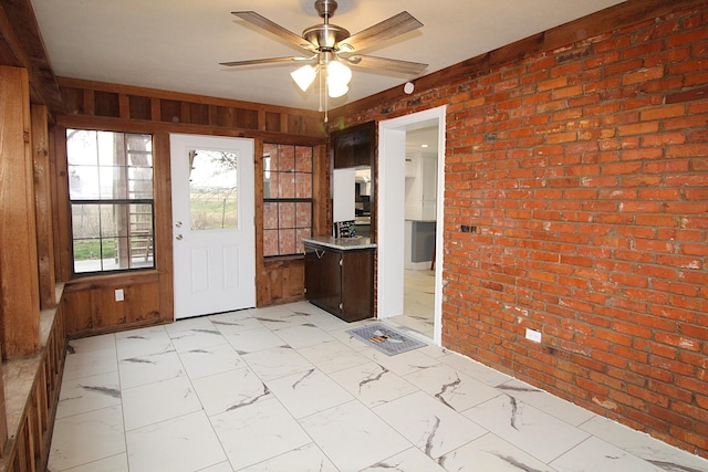 interior space featuring marble finish floor, brick wall, wooden walls, and ceiling fan