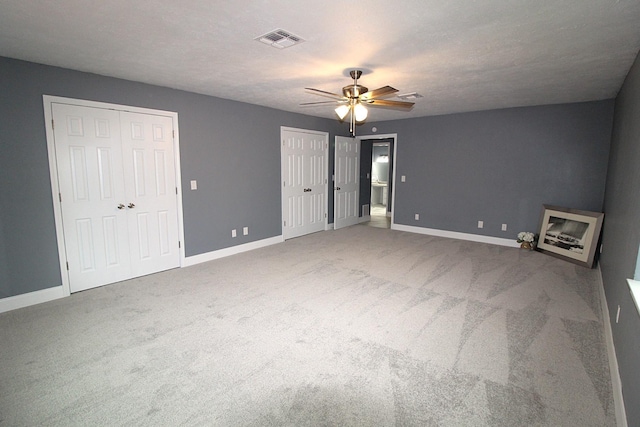 unfurnished bedroom with carpet, two closets, visible vents, and baseboards