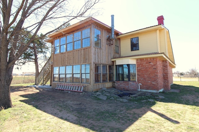 back of house with stairs, a yard, brick siding, and a chimney