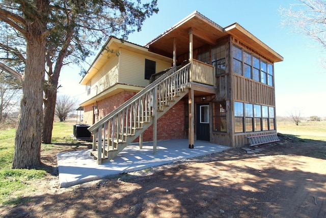 back of house featuring central AC unit, stairway, a patio, and brick siding