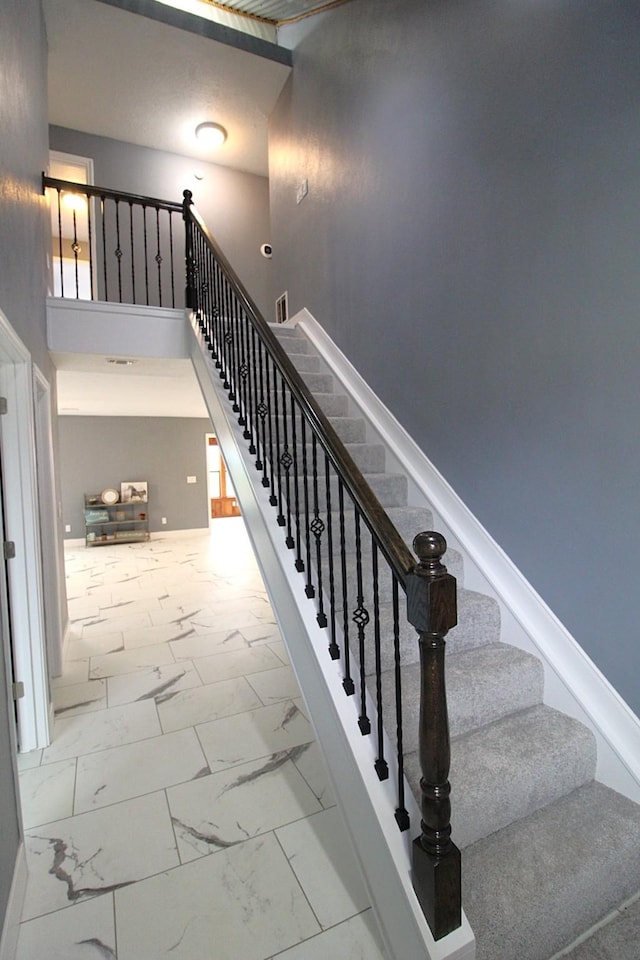 stairs featuring marble finish floor, a towering ceiling, and baseboards