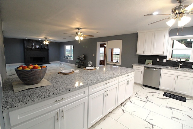 kitchen with a sink, white cabinetry, marble finish floor, stainless steel dishwasher, and a brick fireplace