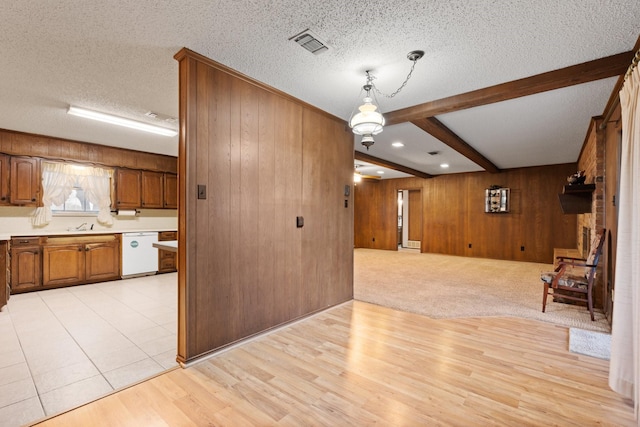 kitchen with beam ceiling, visible vents, brown cabinetry, white dishwasher, and wood walls