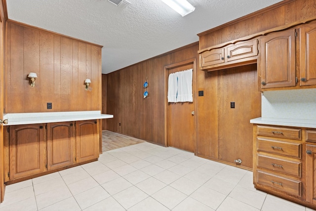 kitchen with a textured ceiling, light countertops, wooden walls, and brown cabinets