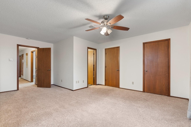 unfurnished bedroom with light colored carpet, a textured ceiling, baseboards, and two closets