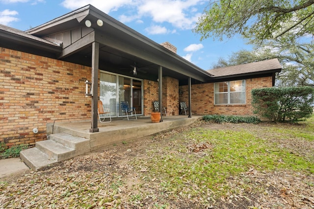 exterior space featuring ceiling fan, brick siding, and a chimney