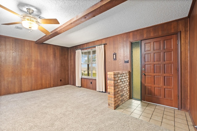 foyer with light tile patterned floors, light colored carpet, a textured ceiling, wood walls, and beam ceiling