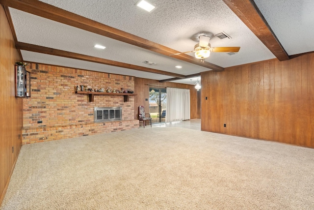 unfurnished living room featuring a textured ceiling, wood walls, a fireplace, carpet flooring, and beamed ceiling