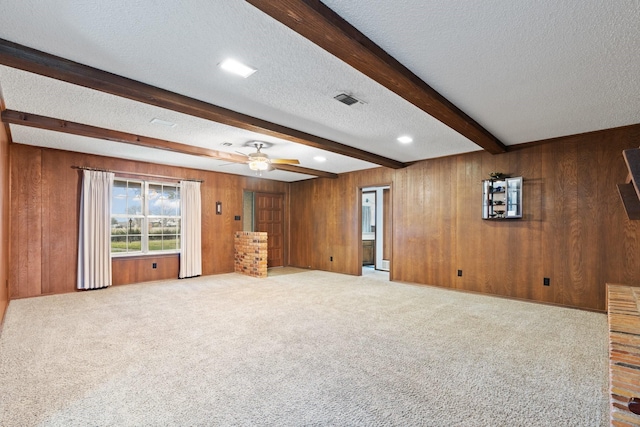 unfurnished living room featuring a textured ceiling, carpet floors, wood walls, visible vents, and beamed ceiling