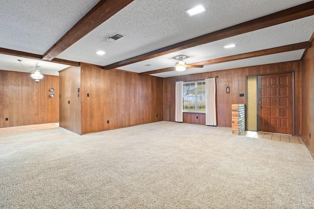 unfurnished living room with a ceiling fan, carpet flooring, wood walls, a textured ceiling, and beamed ceiling